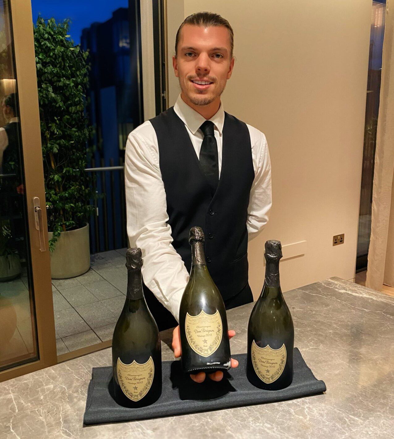 A man in black vest holding three bottles of wine.